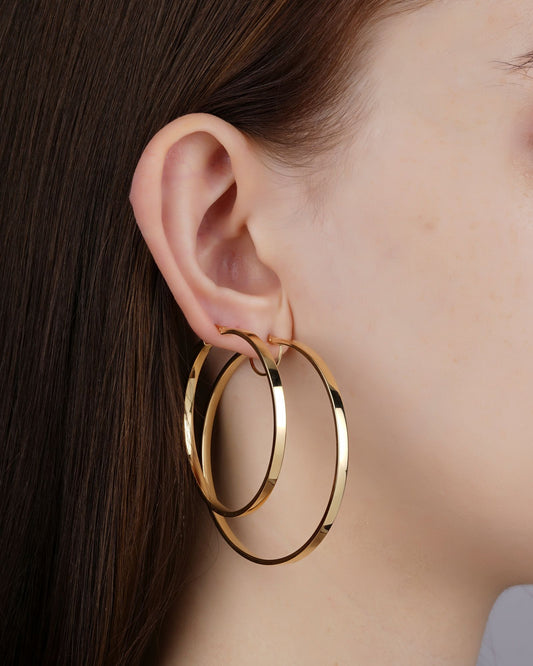 Gros plan sur de grandes créoles dorées portées à l'oreille, illustrant le choix de la taille de boucles d'oreilles