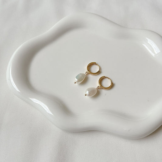 Boucles d'oreilles en or et perles présentées sur une assiette blanche